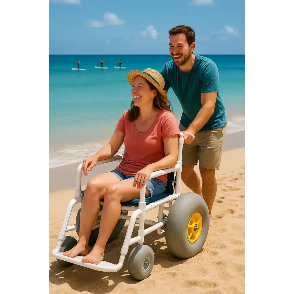 Smiling woman in an Akamai Mobility beach wheelchair with large inflatable tires is pushed along the sandy shore in Lahaina, Maui, with paddleboarders in the background.