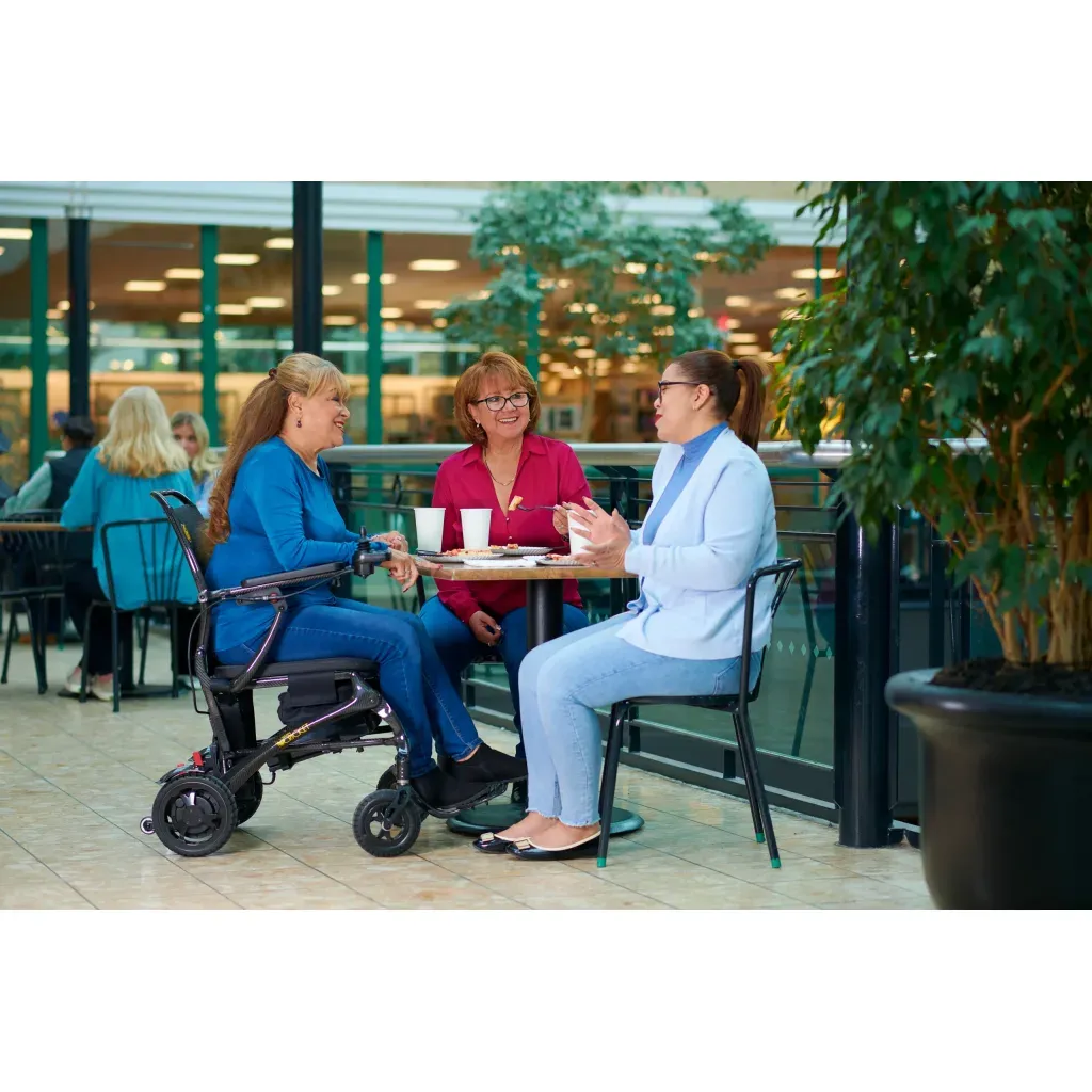 Electric wheelchair user seated at a café table with friends, showing powered mobility for dining and social outings.